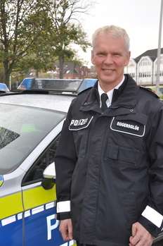Auf dem Bild ist Polizeivizepräsident Jens Eggersglüß vor einem Polizeiwagen zu sehen.