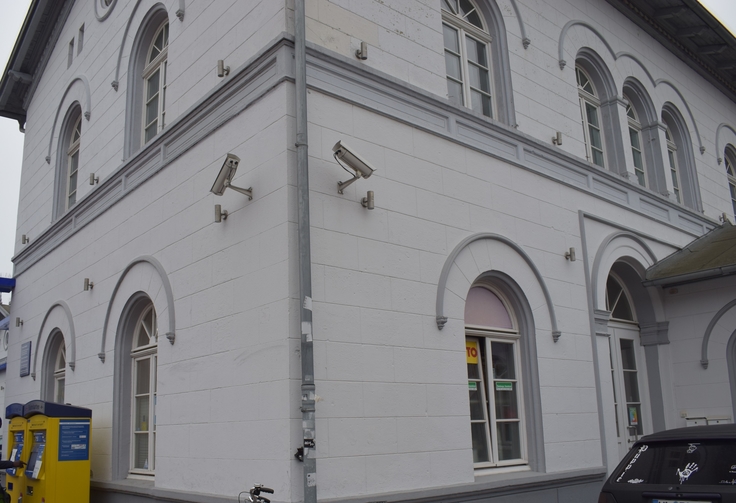 Auf dem Bild ist das Bahnhofsgebäude Winsen (Luhe) mit zwei Überwachungskameras zu erkennen. Die eine, linke Kamera zeigt in Blickrichtung Haupteingang und Fahrkartenautomat. Die andere, rechte Kamera zeigt in Richtung Durchgang zum Gleis.